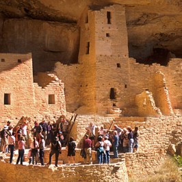 a group of people standing in front of a brick building with Mesa Verde National Park in the background
