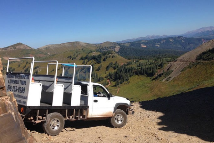 a truck driving down a dirt road in front of a mountain
