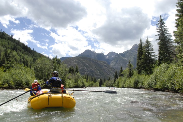 a man riding on the back of a boat next to a lake