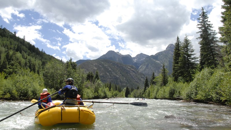 a man riding on the back of a boat next to a lake
